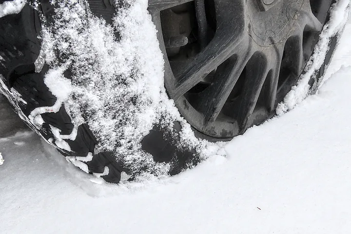 Vinterdäck och fälg som trycker ihop snö framför sig i omkring tio centimeter snö