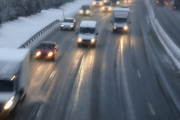 Bilar och lastbilar med tända strålkastare på en isig motorväg i snöigt landskap