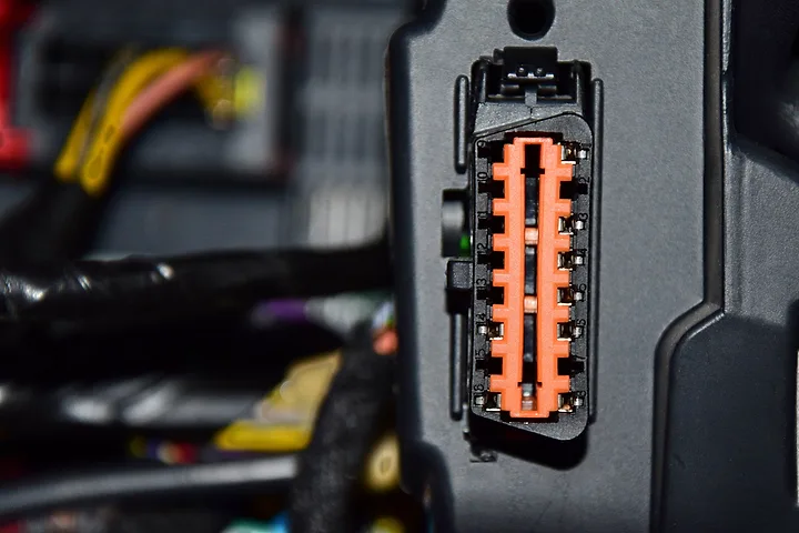 OBD-uttag med orange kontaktdon bland kablage i en bil