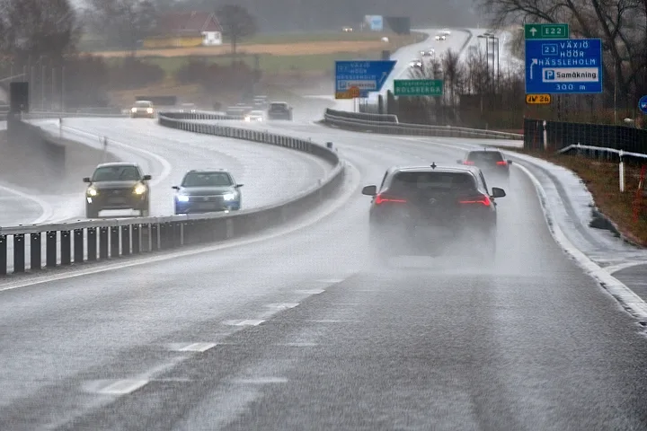 Bilar på en blöt motorväg i regn med vattendimma bakom bilarna