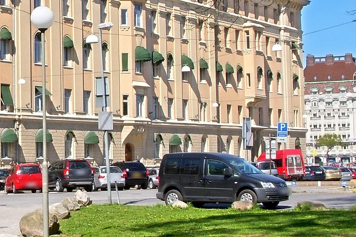 Bilar parkerade längs gatan framför ett stort stenhus, med parkeringsskyltar