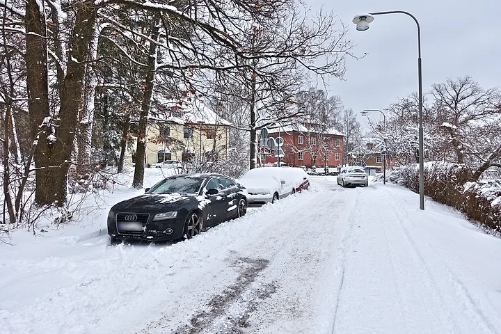 Snötäckta bilar parkerade längs en villagata efter snöfall