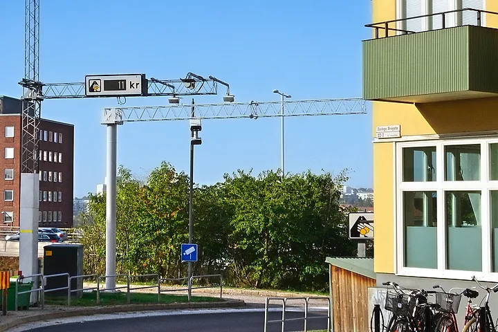 Portal med kameror och en skylt för trängselskatt vid en gata intill ett gult bostadshus