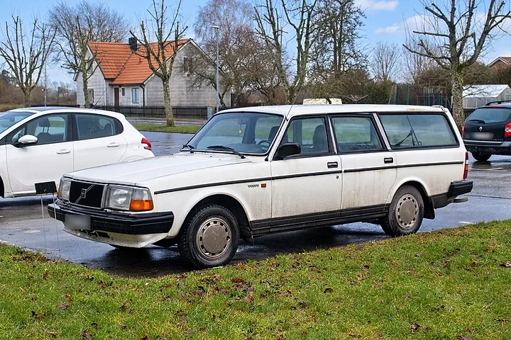 Vit Volvo 245 DL parkerad vid en gräsmatta en mulen vinterdag
